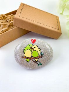 two birds sitting on a branch with a heart painted on the rock next to it