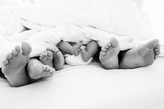 two baby feet laying on top of a bed under a white comforter and blanket