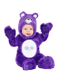 a baby in a purple teddy bear costume sitting on the ground with its arms up