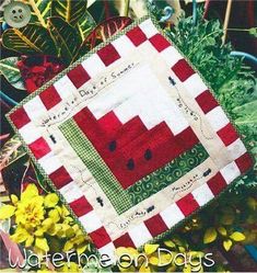 a red and white quilted square with watermelon on it in front of some flowers