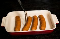 four hot dogs in a red and white dish with a knife sticking out of them