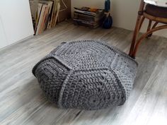 a grey knitted ottoman sitting on top of a wooden floor next to a chair