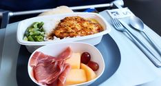 an airplane meal with meat, fruit and vegetables on the tray in front of it