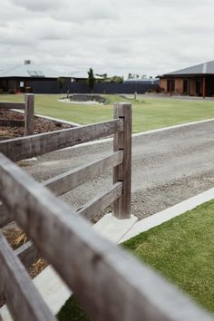 a wooden fence on the side of a road next to a grass field and building