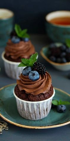 two cupcakes with chocolate frosting and berries on top are sitting on a plate