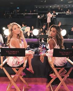 two women sitting in directors chairs at a victoria's secret event with lights on