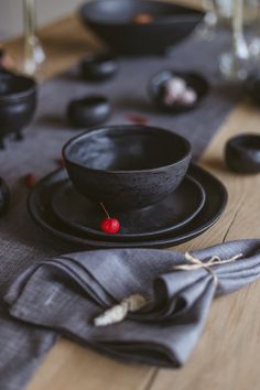 a table with black dishes and napkins on it, including one red berry in the center