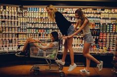 two girls pushing a shopping cart through a grocery store filled with milk and sodas