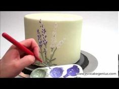 someone is decorating a cake with purple flowers and lavenders on the frosting