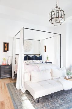 a white bed sitting on top of a wooden floor next to a couch under a chandelier