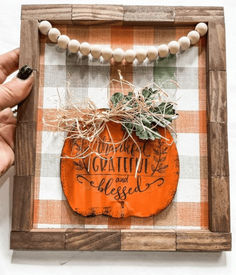 a hand holding an orange pumpkin in a wooden frame