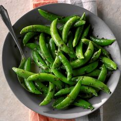 a bowl filled with green beans on top of a table next to a napkin and spoon