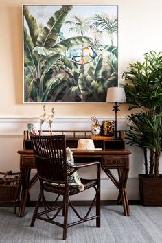 a painting hangs above a desk with a chair and potted plants in front of it