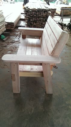 a wooden bench sitting on top of a floor next to piles of wood planks