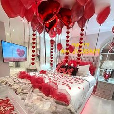 a bed with lots of red heart balloons hanging from the ceiling