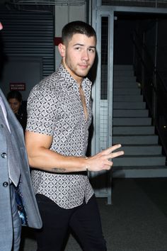 a man in a patterned shirt and black pants is talking to another man with his hand out