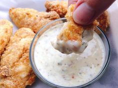 a person dipping something into a small glass bowl filled with ranch dressing and fried chicken wings