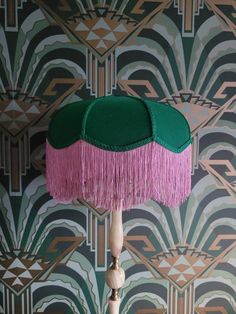 a green and pink table lamp sitting on top of a wooden stand in front of a wall