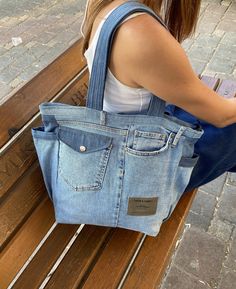 a woman is sitting on a bench with a denim bag in her hand and looking at her phone