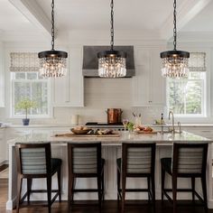 a kitchen with three lights hanging from the ceiling and four chairs in front of it