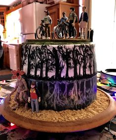 a decorated cake with figurines on top and people standing in the woods around it