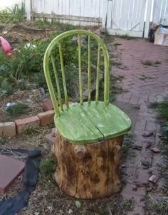 a green chair sitting on top of a tree stump in the grass next to a brick walkway