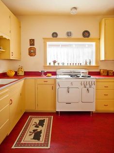 an old fashioned kitchen with yellow cabinets and red flooring on the walls, along with a white stove top oven