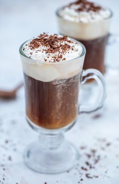 two glasses filled with hot chocolate drink on top of a white countertop next to each other