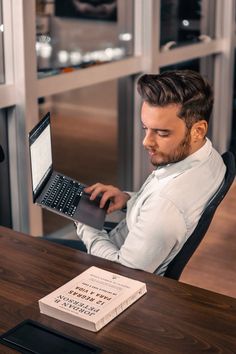 a man sitting at a desk with a laptop computer in front of him and a book on the table