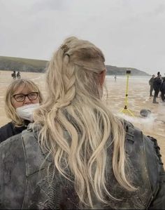 a woman with blonde hair and glasses wearing a face mask standing on the beach in front of other people