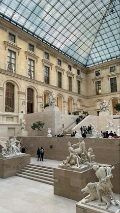 the inside of a building with statues and people walking around it in front of a glass ceiling