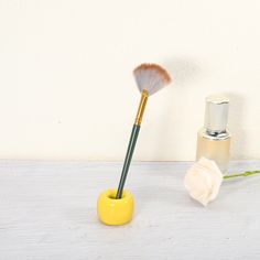 a yellow vase with two brushes in it next to a white rose on a table