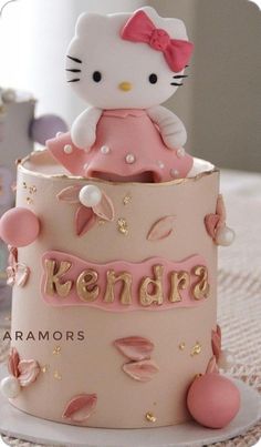 a hello kitty cake with pink frosting and gold decorations on it's top