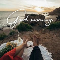 two people sitting on a blanket with the words good morning in front of them and an ocean view