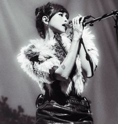 a woman wearing a fur coat singing into a microphone