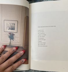 a woman's hand with red and white nail polish holding an open book in front of her