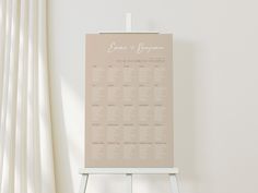 a wedding seating chart on a easel in front of a white curtained window