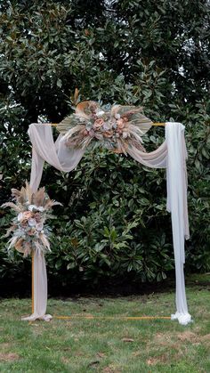 a wedding arch decorated with flowers and greenery in the middle of a lawn area