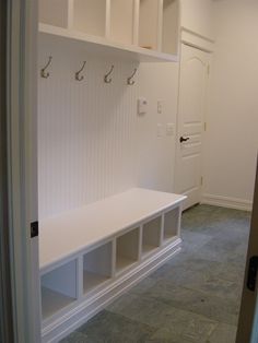 a white bench sitting in the middle of a room with hooks on it's wall