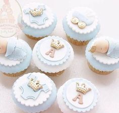 six cupcakes decorated with blue frosting and gold trimmings are arranged on a white surface