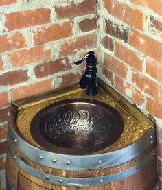 a wooden barrel with a metal sink in it next to a brick wall and a faucet