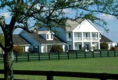 a large white house sitting on top of a lush green field next to a wooden fence