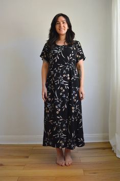 a woman standing in front of a white wall wearing a black dress with flowers on it