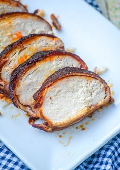 slices of meat sitting on top of a white plate next to a blue and white checkered table cloth