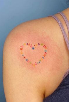 a woman's back with a small heart tattoo on her left shoulder and the word love written in smaller letters