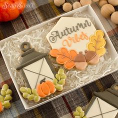 two decorated cookies in a box on a table next to nuts and pumpkins with the word autumn written on them