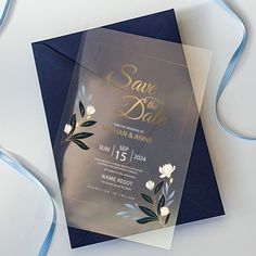 a wedding card with flowers on it and blue ribbon around the edge, sitting on top of a white table