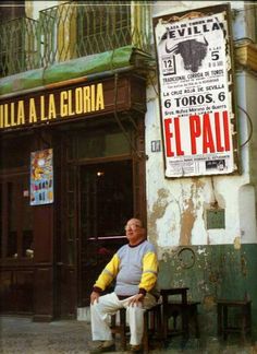 a man sitting on a bench in front of a building with a sign above it