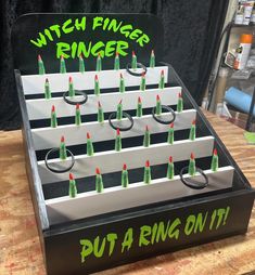 Celebrate your spooky get-together by flinging rings on witchy fingers! Ring Toss Carnival Game measures approximately 24"x24" and comes with 6 rings.  Front panel opens to allow easy access to rings inside. We offer color choice and custom graphics with your name or logo at no extra charge (in most cases) Pro quality carnival game built in the USA from sturdy, cabinet grade 3/4" maple plywood.  (not flimsy pressboard like some of our competitors)  We have been in business since 2009 and have cr Carnival Ring Toss Game, Inexpensive Halloween Party Decorations, Halloween Booths Games, Ring Toss Halloween Game, Ghost Blast Game, Eyeball Toss Halloween Game, Halloween School Table Decorations, Candy Corn Ring Toss Game, Whats In The Box Game Ideas Halloween