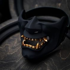 a black mask with gold teeth and fangs on it's face is sitting on a table